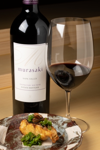 A bottle of red murasaki wine accompanied by a glass of red wine with a salmon dish with garnish from Kenzo Napa restaurant